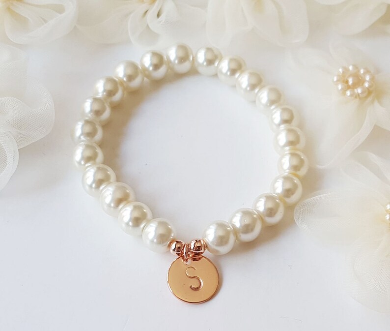 May include: A white pearl bracelet with a gold charm featuring the letter 'S'.