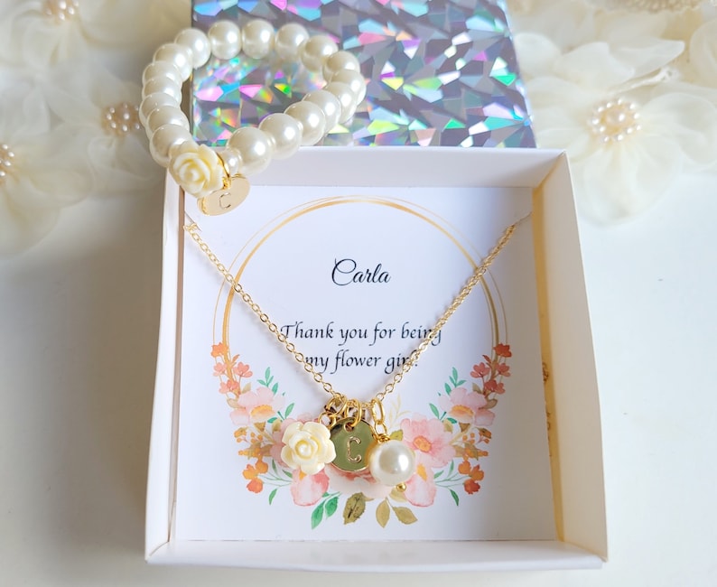 K&ouml;nnte beinhalten: Eine wei&szlig;e Geschenkbox mit einer goldenen Halskette und einem Perlenarmband. Die Box enth&auml;lt eine Karte mit der Aufschrift "Carla, Danke, dass du meine Blumenm&auml;dchen bist".