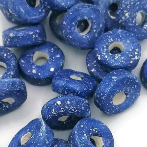 Pode incluir: Um monte de contas de cerâmica azul em forma de rosquinha com manchas brancas. As contas estão espalhadas sobre uma superfície branca.