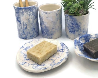 May include: A bathroom set with a blue and white speckled design. The set includes a toothbrush holder, a tumbler, a soap dish, and a small planter. The soap dish has a bar of brown soap and the planter has a small green succulent plant.