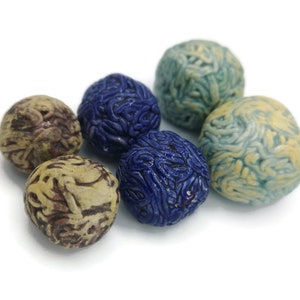 Puede incluir: Seis esferas de cerámica en varios colores, incluyendo azul, beige y amarillo. Cada esfera tiene una superficie texturizada, similar a un cerebro. Las esferas están dispuestas sobre un fondo blanco.