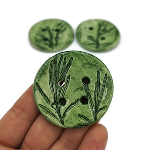 May include: Three green ceramic buttons with a leafy design. The buttons have three holes each.