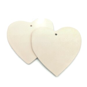 May include: Two off-white heart-shaped ornaments with a matte finish. Each heart has a small hole at the top for hanging. The hearts are slightly textured and appear to be made of a solid material.