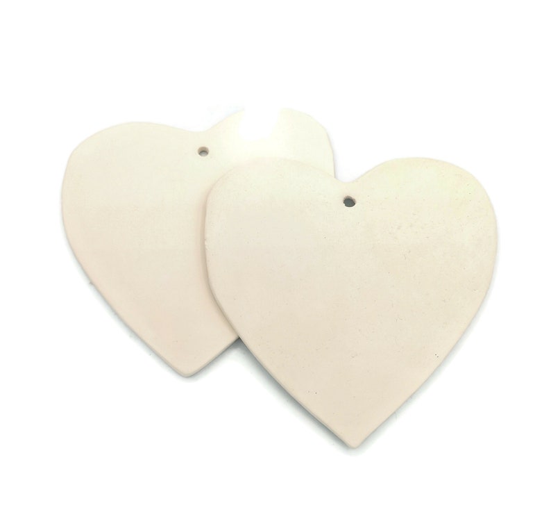 May include: Two off-white heart-shaped ornaments with a matte finish. Each heart has a small hole at the top for hanging. The hearts are slightly textured and appear to be made of a solid material.