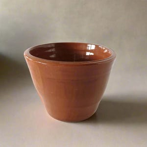 Può includere: Un vaso in ceramica di colore terracotta con fondo arrotondato e bordo leggermente svasato.