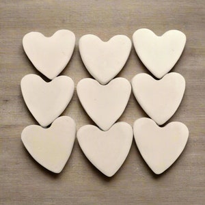 May include: Nine off-white heart-shaped objects arranged in a grid pattern. The hearts are smooth and appear to be made of a solid material. The background is a light brown, wood-grain surface.