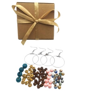 May include: A set of three silver hoop earrings with a brown cardboard box tied with a gold ribbon. The box contains a variety of colorful beads, including blue, brown, pink, and yellow.
