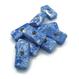 May include: A group of eight blue ceramic rectangular beads with a hole in the centre of each bead. The beads have a marbled pattern with white and blue swirls.