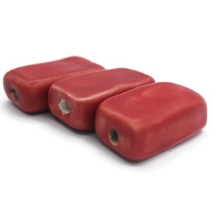 Peut inclure: Trois perles rectangulaires en céramique rouge avec un trou au centre de chaque perle.