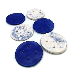 May include: Six ceramic buttons in shades of blue and white. The blue buttons are a solid colour, while the white ones feature a speckled blue pattern. Each button has three holes for sewing.