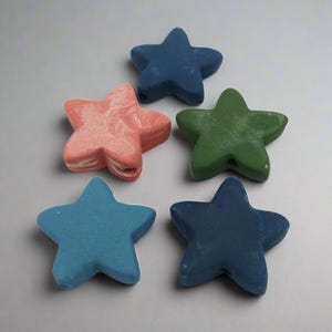 May include: Five star-shaped beads in various colors: coral, blue, green, and navy. Each bead has a hole for stringing. The beads are made of a solid material and have a slightly textured surface. Ideal for jewelry making or craft projects.