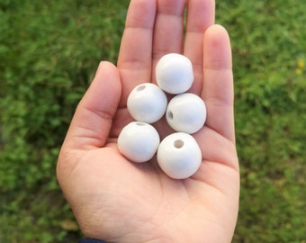 May include: A hand holding six white wooden beads with holes in the center.