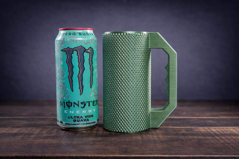 Peut inclure: Une canette de Monster Energy Ultra Vice Guava turquoise avec une marque et du texte noirs &agrave; c&ocirc;t&eacute; d'une tasse cylindrique vert olive dot&eacute;e d'un ext&eacute;rieur textur&eacute; &agrave; motif losange et d'une grande poign&eacute;e angulaire dentel&eacute;e.