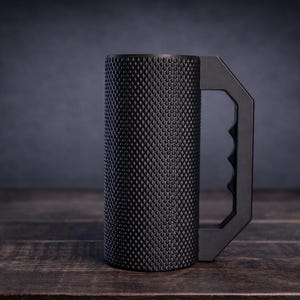 Peut inclure: Une tasse cylindrique noir mat dot&eacute;e d'une surface ext&eacute;rieure textur&eacute;e &agrave; motif de losanges. La tasse comprend une poign&eacute;e angulaire solide avec une prise int&eacute;rieure profil&eacute;e, offrant une apparence industrielle distincte &agrave; ce r&eacute;cipient.
