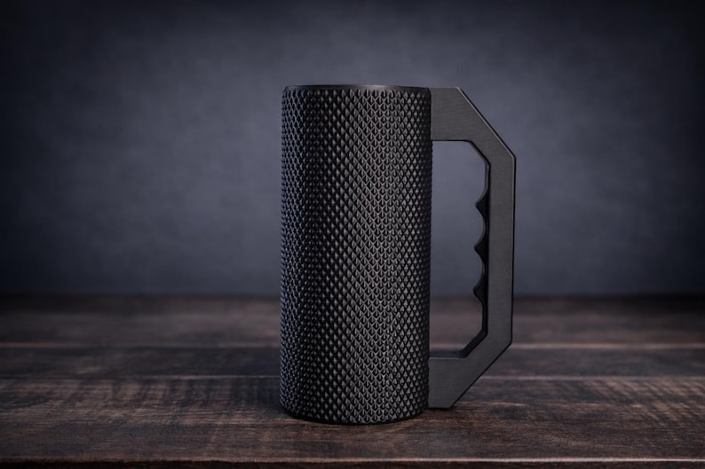 Peut inclure: Une tasse cylindrique noir mat dot&eacute;e d'une surface ext&eacute;rieure textur&eacute;e &agrave; motif de losanges. La tasse comprend une poign&eacute;e angulaire solide avec une prise int&eacute;rieure profil&eacute;e, offrant une apparence industrielle distincte &agrave; ce r&eacute;cipient.
