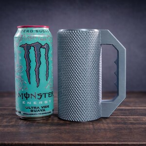 Peut inclure: Une canette Monster Energy Ultra Vice Guava turquoise avec un logo et du texte noirs &agrave; c&ocirc;t&eacute; d'une chope cylindrique en m&eacute;tal gris avec un ext&eacute;rieur textur&eacute; &agrave; motif losange et une grande poign&eacute;e angulaire avec une prise dentel&eacute;e.