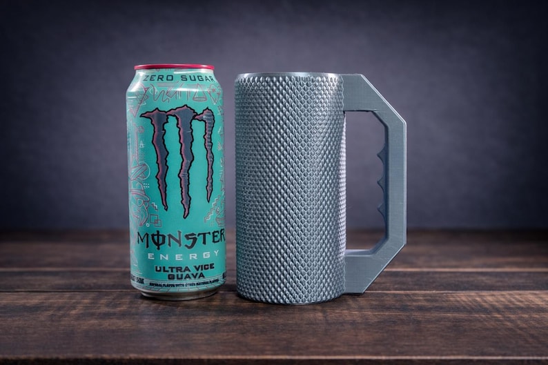 Peut inclure: Une canette Monster Energy Ultra Vice Guava turquoise avec un logo et du texte noirs &agrave; c&ocirc;t&eacute; d'une chope cylindrique en m&eacute;tal gris avec un ext&eacute;rieur textur&eacute; &agrave; motif losange et une grande poign&eacute;e angulaire avec une prise dentel&eacute;e.