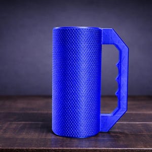 Peut inclure: Un mug cylindrique bleu pr&eacute;sentant une texture molet&eacute;e en losanges sur toute sa surface ext&eacute;rieure. Le mug est dot&eacute; d'une grande poign&eacute;e g&eacute;om&eacute;trique angulaire avec une s&eacute;rie de prises pour les doigts sur le bord int&eacute;rieur.