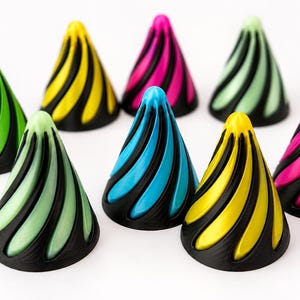 May include: A collection of eight cone-shaped objects featuring a black base with a spiraling, raised pattern in vibrant colors including lime green, bright yellow, hot pink, pale mint green, and electric blue, arranged on a white surface.