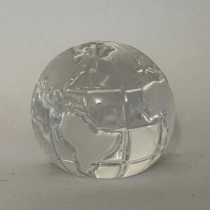 May include: A clear glass globe with etched continents. The spherical decorative object is transparent and reflects light, showcasing the world map. The globe is a decorative item, suitable for display on a desk or shelf.