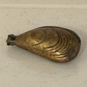 May include: A vintage brass clam shell-shaped object with a hinged top. The shell has etched lines and a tarnished, aged appearance. The object is likely a decorative piece or a small container.