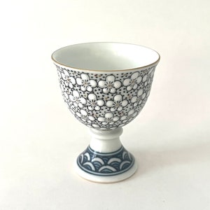 May include: A white ceramic cup with a black and white floral pattern and a blue and white wave pattern on the base.