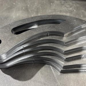 Puede incluir: Una pila de cinco piezas de metal, cada una con una forma curva y un agujero en el centro. Las piezas están apiladas una encima de la otra, con la pieza más grande en la parte inferior y la pieza más pequeña en la parte superior.