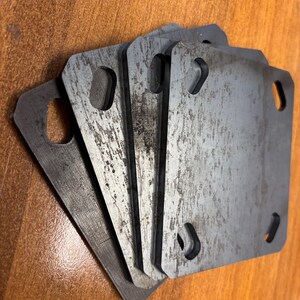 May include: Five metal plates with rounded corners and a hole in the center. The plates are stacked on top of each other and have a worn, metallic finish.