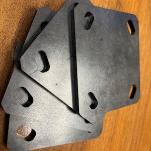 May include: Four black metal plates with rounded corners and cut-out circles. The plates are stacked on top of each other.
