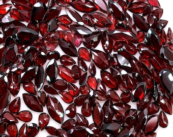 May include: A large collection of loose, faceted deep red garnet gemstones in various shapes, including marquise, pear, and round cuts. Each stone features multiple polished surfaces that reflect light, creating a vibrant, dark red appearance.