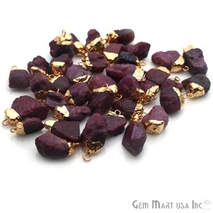 May include: A collection of raw ruby gemstone pendants with gold accents. Each pendant has a gold bail for easy attachment to jewelry making projects.