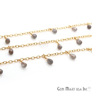 Puede incluir: Un collar de cadena dorada con múltiples hebras y cuentas de piedras preciosas grises colgantes. El collar está sobre un fondo blanco.