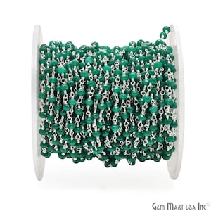 May include: A spool of green gemstone beads strung on a silver chain. The chain is made of small, linked silver rings. The beads are faceted and have a dark green color.