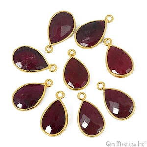 May include: Eight teardrop-shaped ruby gemstone pendants with gold-colored bezels and loops. The faceted, deep red stones are set in a gold frame, creating a luxurious look. Ideal for jewelry making.