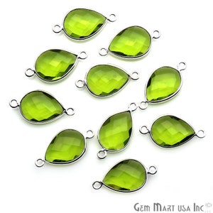 May include: A collection of ten pear-shaped, faceted green gemstones with silver-colored metal frames and small loops for jewelry making. The gemstones are a vibrant, light green color and are arranged on a white background.