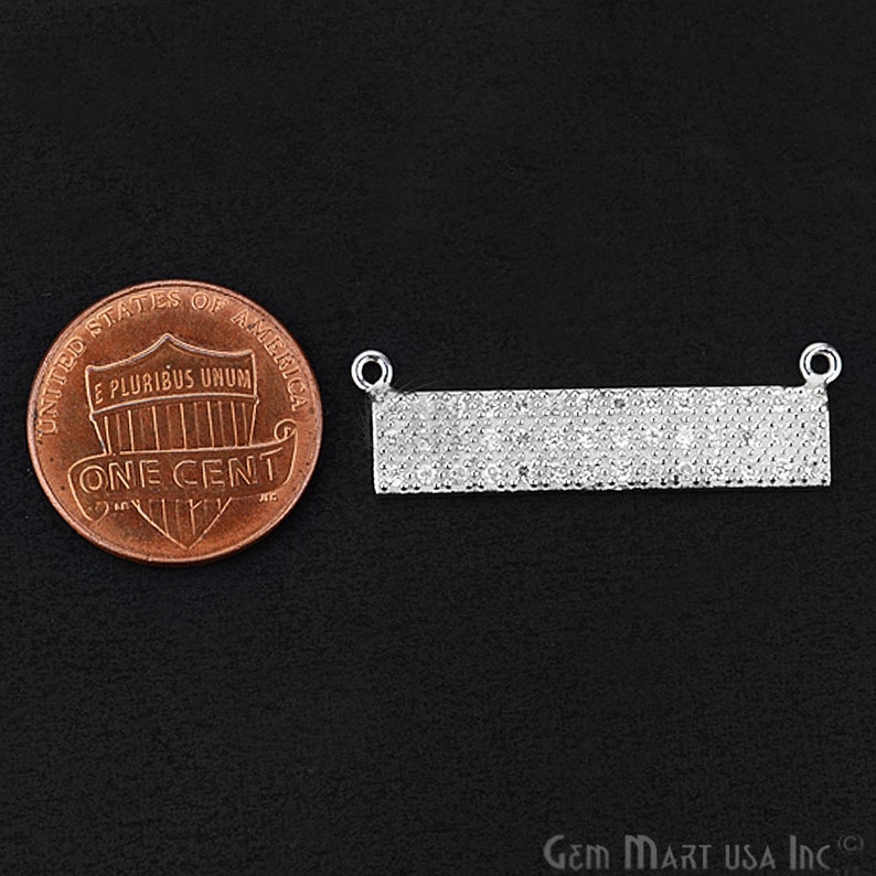 May include: A silver bar pendant with a pave setting of small clear stones. The pendant is shown next to a US penny for size comparison.