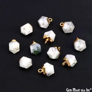 May include: A collection of gemstone pendants with a hexagonal shape. The pendants are white with black veining and gold-colored metal accents. One pendant has green inclusions. The pendants are displayed on a black surface.