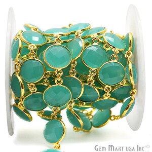 May include: A gold chain with round, teal green gemstone beads. The chain is coiled on a white spool. Gem Mart USA Inc. is printed on the spool.