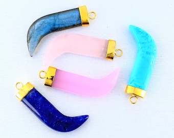 Puede incluir: Una colección de colgantes en forma de cuerno en varios colores, incluyendo azul, rosa y turquesa. Cada colgante tiene una tapa de metal dorado con un lazo para sujetar a una cadena. Los colgantes están hechos de piedra pulida.