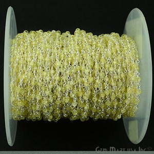 May include: A spool of yellow citrine gemstone beads strung on a silver chain. The chain is made of small, delicate links. The beads are faceted and have a light, translucent appearance.