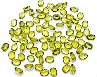 May include: A collection of 50 loose peridot gemstones, each cut into an oval shape. The peridots are a vibrant green color and are scattered on a white background.