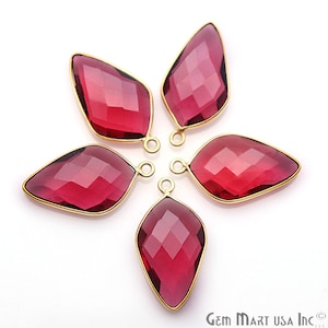 Puede incluir: Seis colgantes de piedra roja con engastes de metal dorado. Las piedras preciosas son facetadas y tienen forma de lágrima. Los colgantes están dispuestos en forma de estrella.