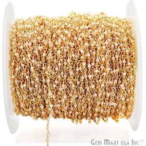 May include: A spool of gold-toned chain with small white beads. The chain is used for jewellery making.