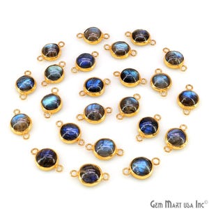 May include: A collection of round labradorite gemstones set in gold-toned metal bezels, each featuring two small loops on opposite sides. The stones display iridescent blue and grey flashes against a dark base, arranged in a scattered pattern.