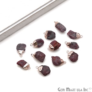 May include: Twelve raw ruby gemstone pendants with rose gold plated jump rings. The ruby gemstones are various shapes and sizes.