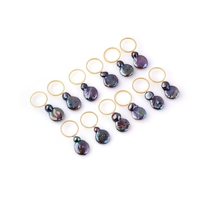 May include: Ten gold rings with black pearl accents. Each ring has a single pearl attached to it. The pearls are iridescent and have a dark, almost black, color.