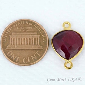 May include: Gold-tone heart-shaped pendant with a red gemstone. The pendant is shown next to a US penny for size comparison.