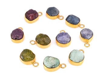 May include: A collection of ten gemstone pendants in various colors, including purple, green, and blue. Each stone is set in a gold-colored bezel with a small loop for attaching to a chain or other jewelry component. The pendants are arranged in a circular pattern.