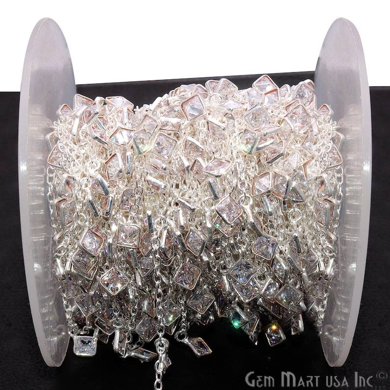 K&ouml;nnte beinhalten: Eine Spule mit silberner Kette mit klaren quadratischen Kristallen. Die Kette ist um eine transparente Kunststoffspule gewickelt.