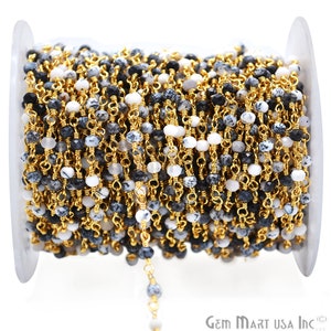 May include: A spool of gold chain with black and white gemstone beads. The chain is made of gold-plated metal and the beads are approximately 4mm in diameter. Gem Mart USA Inc. is printed on the spool.